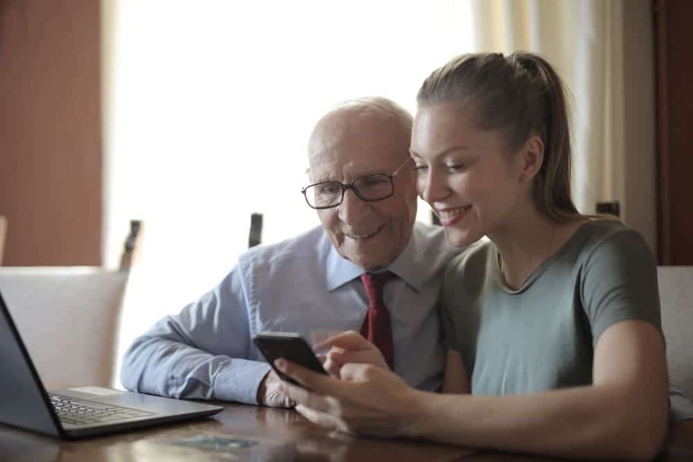 Younger person teachers elderly man how to use a smartphone